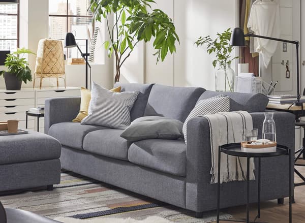 A gray sofa in a living room with a round black side table next to it and potted plants behind it.