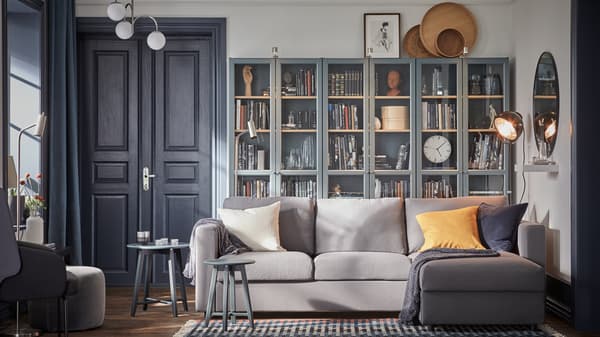 A gray sofa with chaise longue, three gray turquoise bookcases with glass doors with plenty of books in them.