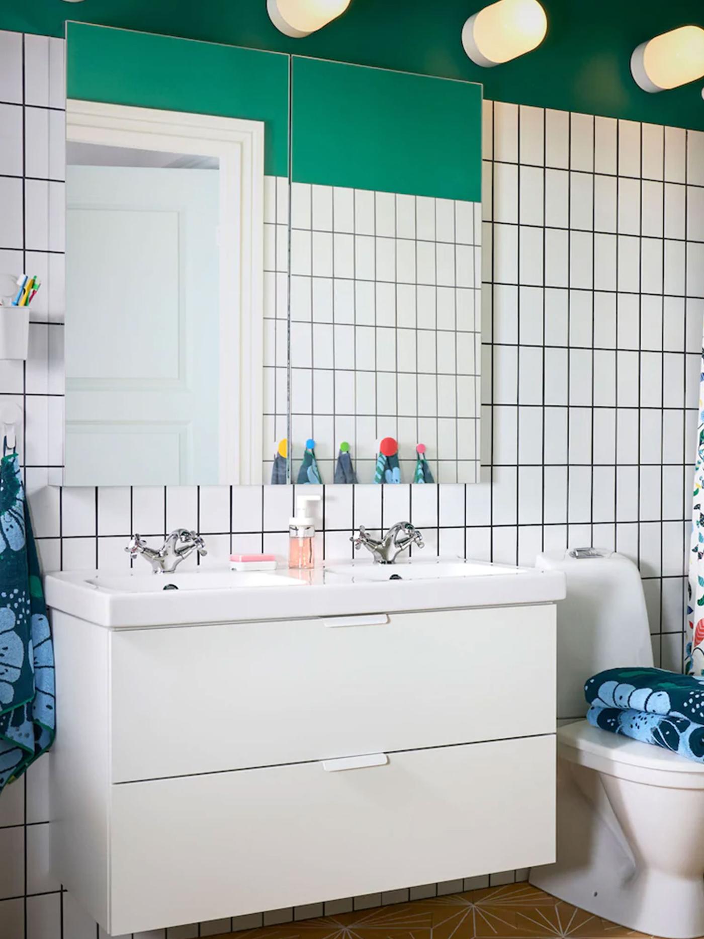 A green bathroom with white tiling and a large mirror above a white double washstand with two drawer.