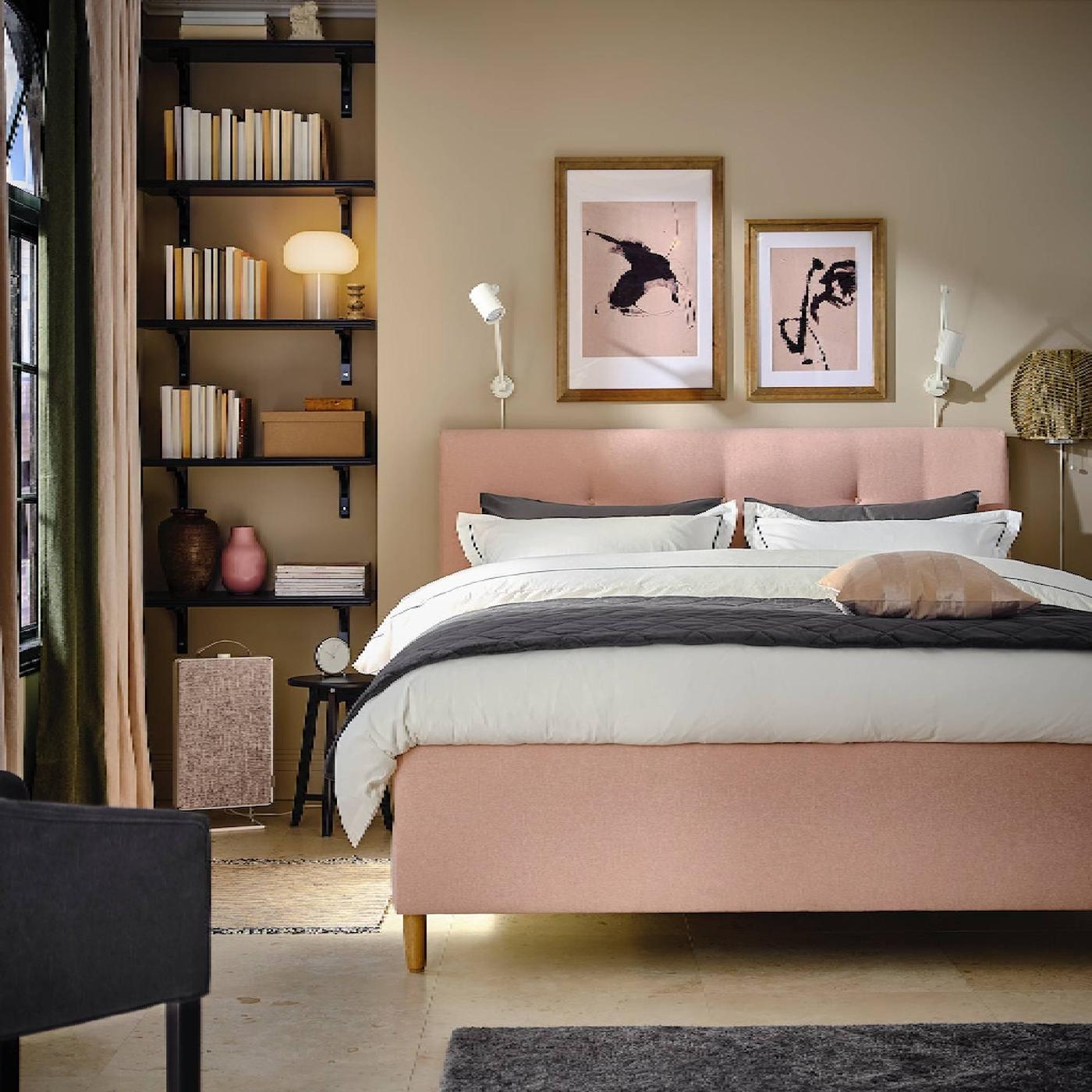 A green bedroom with a dark green upholstered bed covered in white bed linen. A black work lamp is on a bedside table.