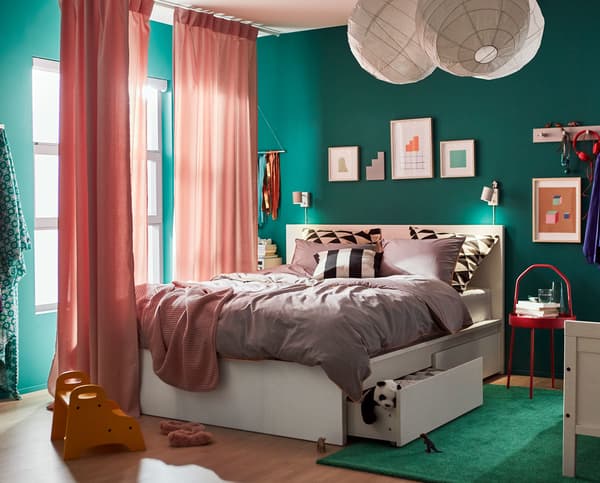 A green bedroom with white, doubled bed that has storage underneath.