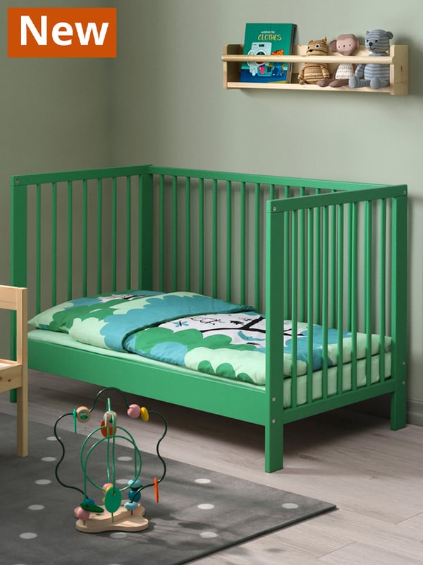 A green GULLIVER cot for baby and children in a children's room setting. A colourful cot linen cover is placed within the cot.