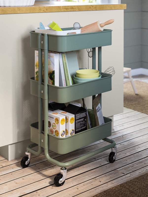 A green kitchen cart with baking and cooking accessories and cookbooks in a kitchen.