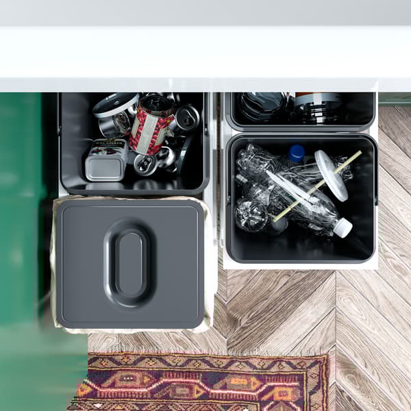 A green kitchen with an open cabinet where VARIERA waste sorting bins in black are pulled out to show how to recycle.