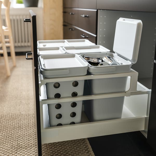 A green kitchen with an open cabinet where VARIERA waste sorting bins in black are pulled out to show how to recycle.