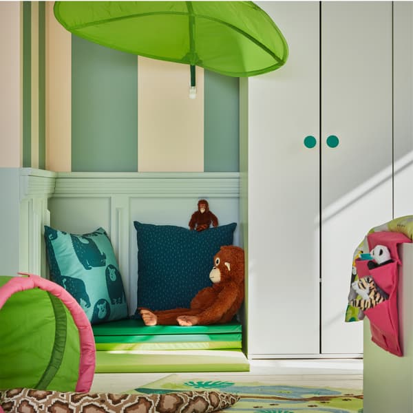 A green leaf-shaped canopy mounted on a wall, a white wardrobe and a folded green gym mat on the floor.