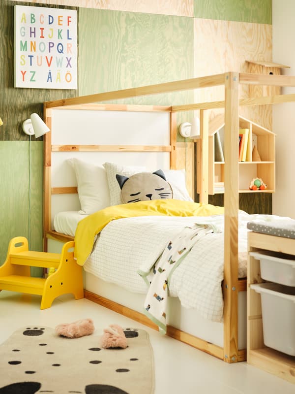 A green room with white cupboards where a child lies on the carpet and plays with Lego.