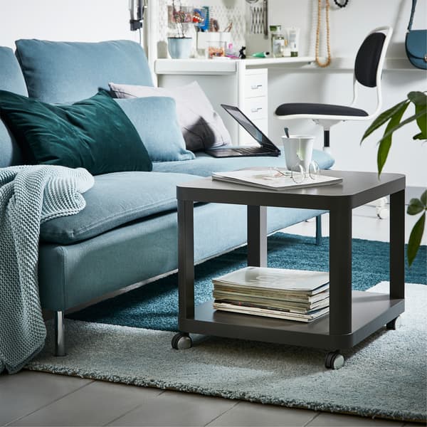 A green sofa and a gray coffee table on castors are standing on a two-colored light blue/green rug.