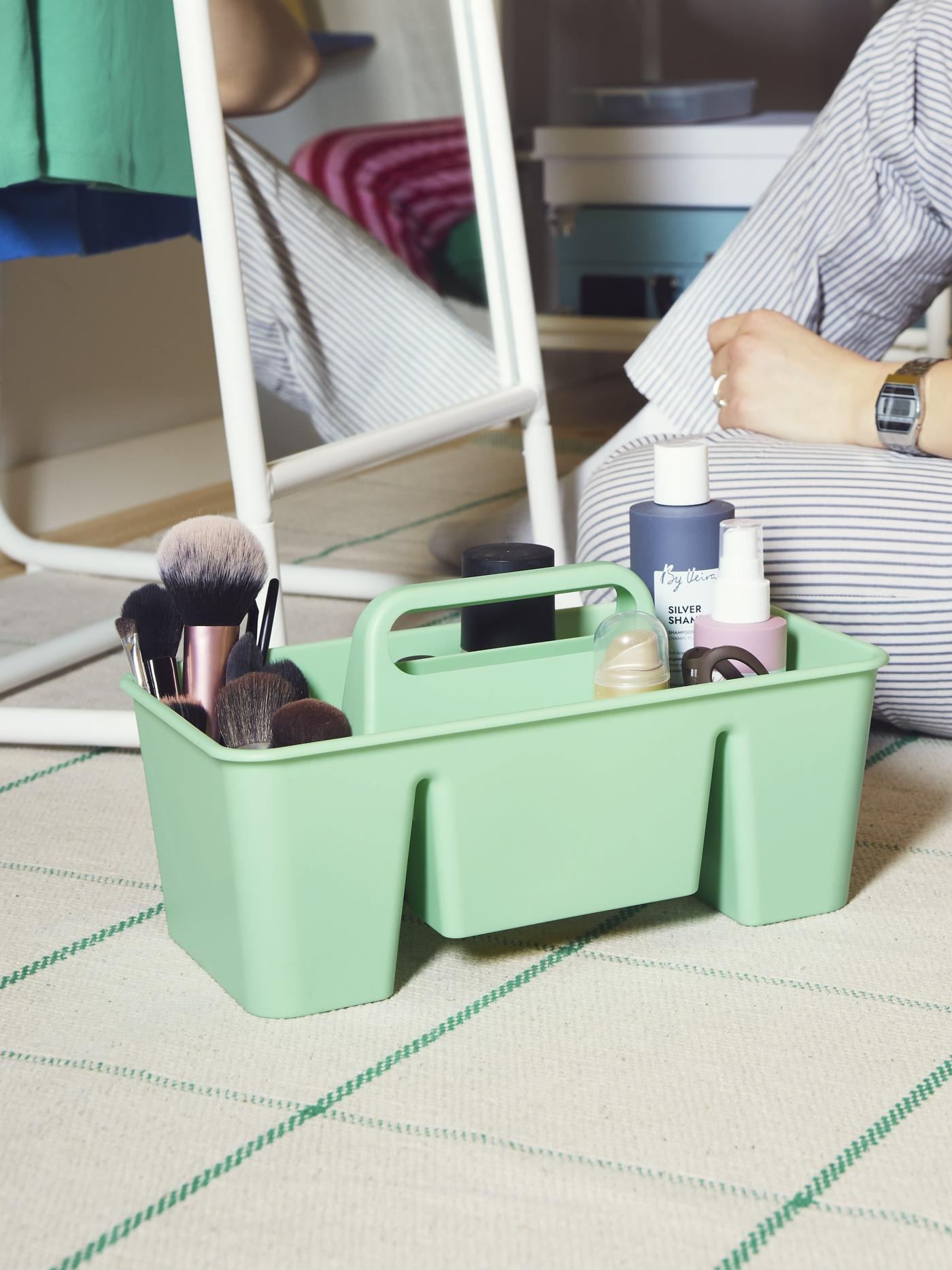 A green STACKSTOD desk organiser on the floor with makeup products inside