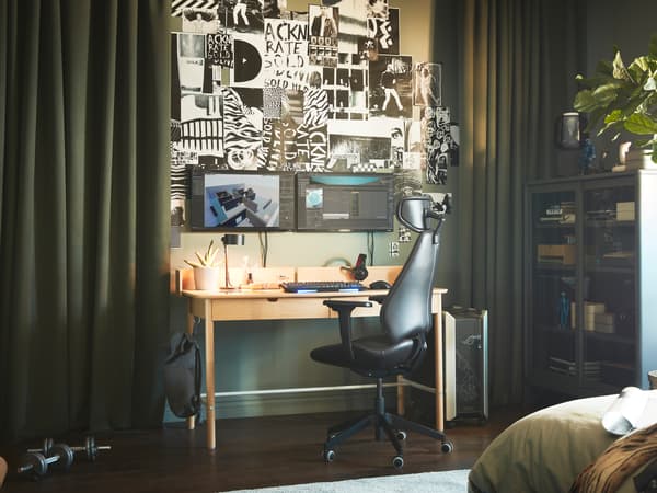 A green-themed room with a RIDSPÖ oak-veneer desk by dark-green ROSENMANDEL curtains, opened to reveal screens and wall art.