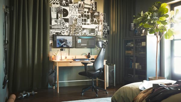 A green-themed room with a RIDSPÖ oak-veneer desk by dark-green ROSENMANDEL curtains, opened to reveal screens and wall art.