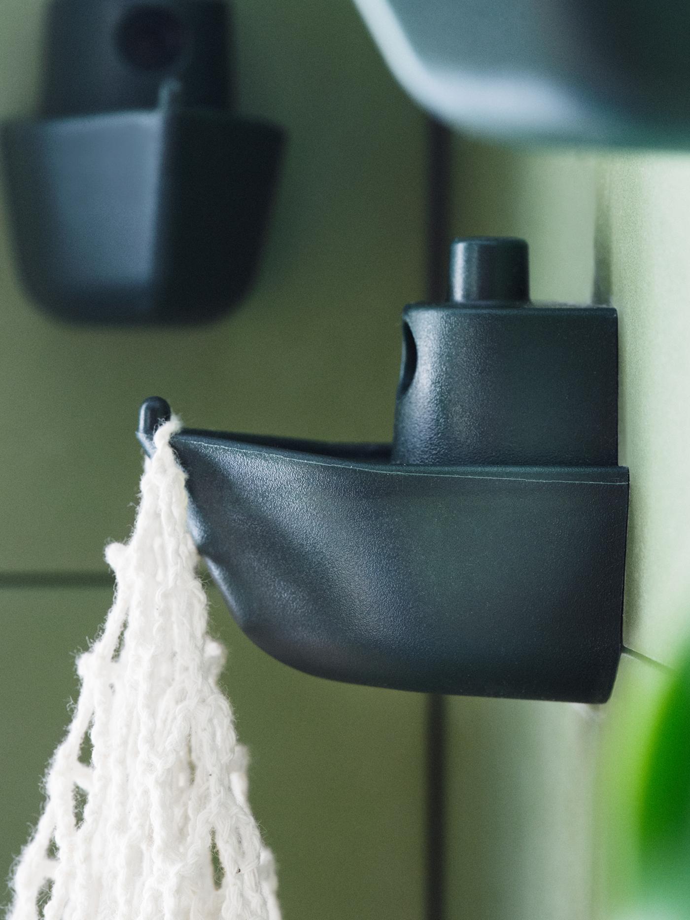 A green tile wall with three green KNOPARE hooks resembling a toy boat, one of which is holding a white macrame bag.