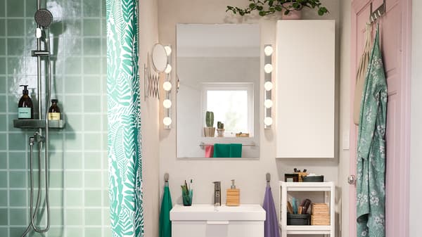 A green tiled shower next to a pink room with a white wash-basin and wall cabinet. Two illuminated LEDSJÖ wall lamps.