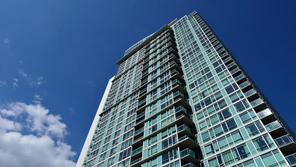 A grey and green apartment building with corner balconies and windows facing an overcast sky.