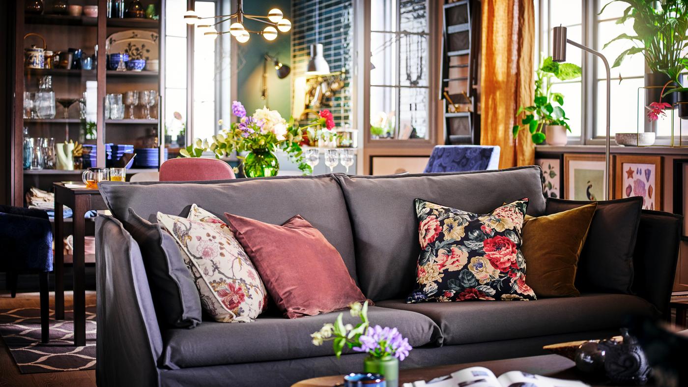 A grey BACKSÄLEN sofa with four scatter cushions in front of a dining table and chairs with framed art on the wall.