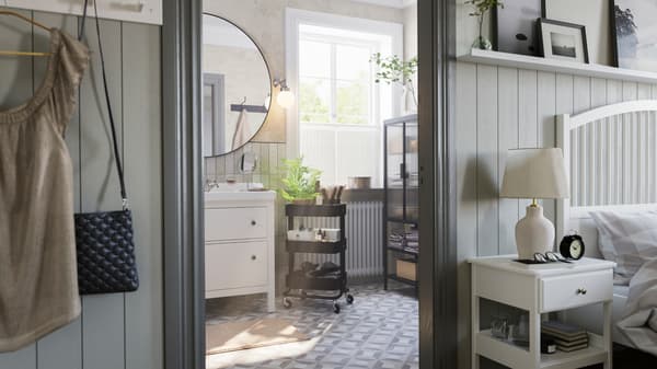 A grey bathroom with a big window has a white HEMNES washstand, a black RÅSKOG trolley and a MOSSJÖN glass door cabinet.