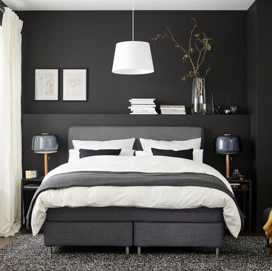 A grey bed in a room with dark walls.