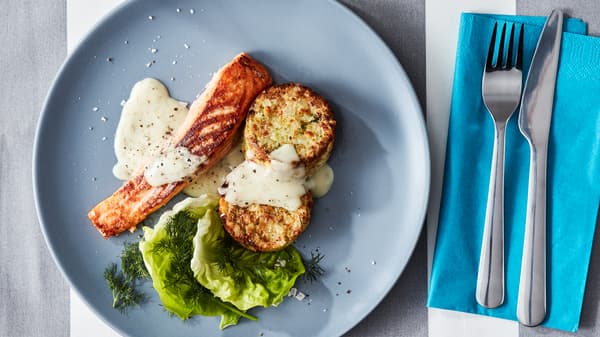 A grey-blue plate of SJÖRAPPORT salmon fillet with salad, sauce, GRÖNSAKSKAKA vegetable medallions and DRAGON cutlery.