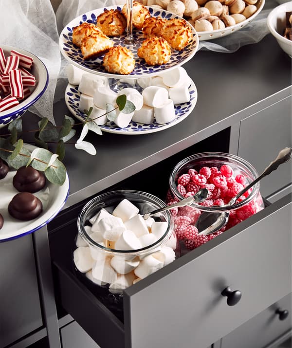 A grey chest of drawers with an open drawer containing two large jars filled with festive candy. 