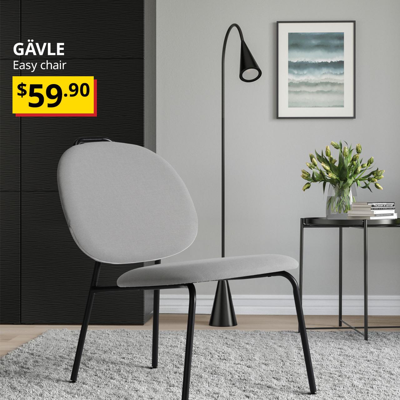 A grey GÄVLE easy chair placed next to a side table and a standing lamp in a reading corner in a room setting. Black text overlay image on the left that reads, "GÄVLE, Easy chair" with the BTI price in yellow/red and black text: $59.90.