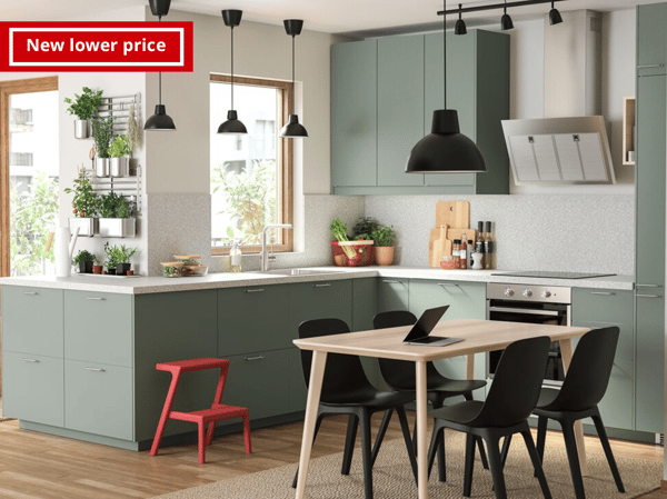 A grey-green kitchen, a wooden dining table, black chairs, a black pendant lamp and lots of herbs that hang on rails.
