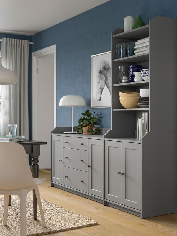 A grey HAUGA combination of a chest of drawers side by side with a high cabinet, standing by a living room wall.