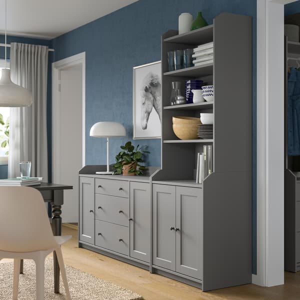 A grey HAUGA combination of a chest of drawers side by side with a high cabinet, standing by a living-room wall.