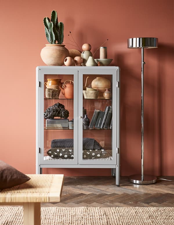 A grey IKEA FABRIKÖR glass-door cabinet displays decorative items in a living room.