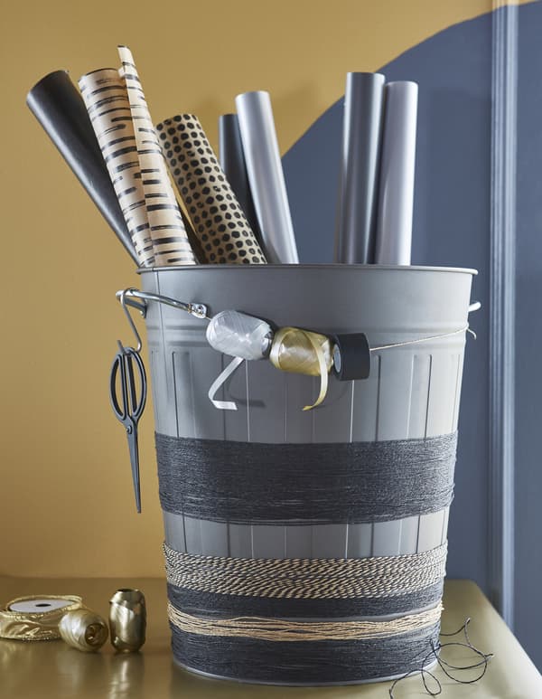 A grey KNODD bin holds wrapping paper rolls, as well as twine wrapped around the base, and spools of ribbon.