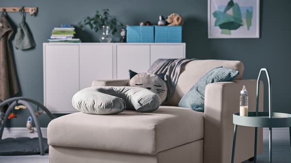 A grey LEN nursing pillow on a beige VIMLE chaise longue, beside a light grey-green BURVIK side table with a feeding bottle.
