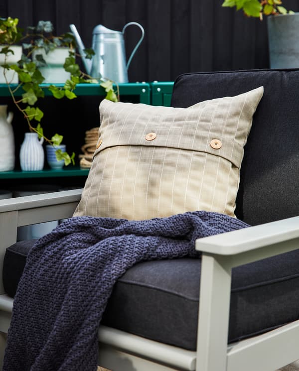 A grey outdoor armchair with back and seat cushions in dark grey, a beige outdoor cushion and a dark grey throw.
