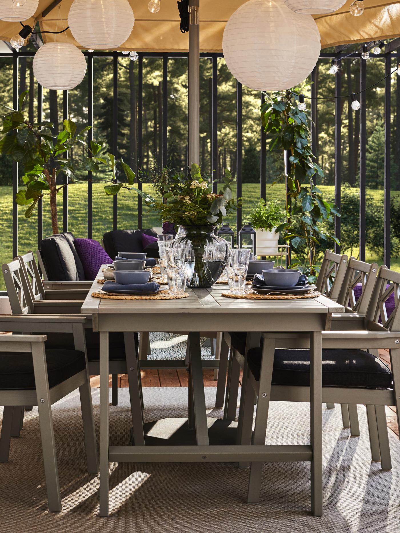 A grey outdoor table and six grey chairs with armrests and black seat cushions. The table is set with blue dinnerware.