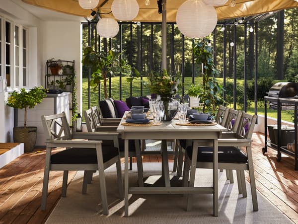 A grey outdoor table and six grey chairs with armrests and black seat cushions. The table is set with blue dinnerware.