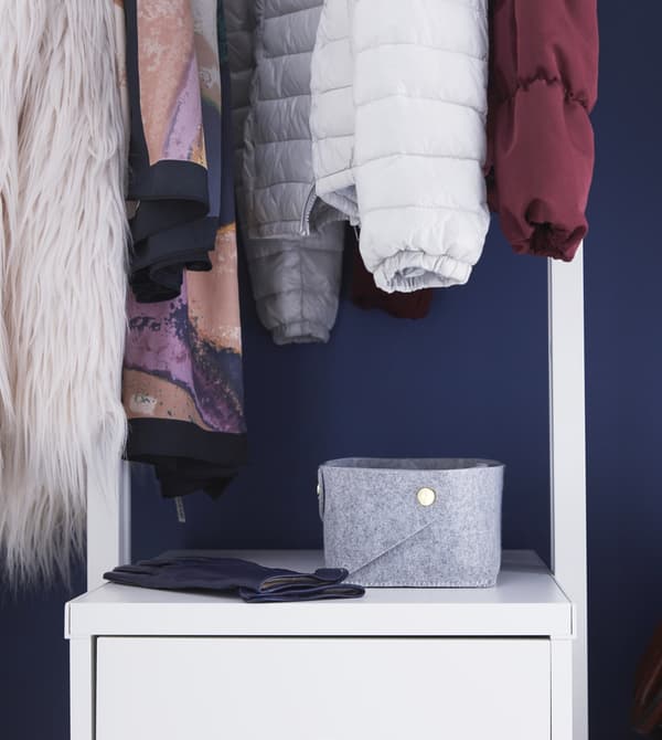 A grey PUDDA felt basket on a cabinet under jackets hanging from a clothes rail in the hall.