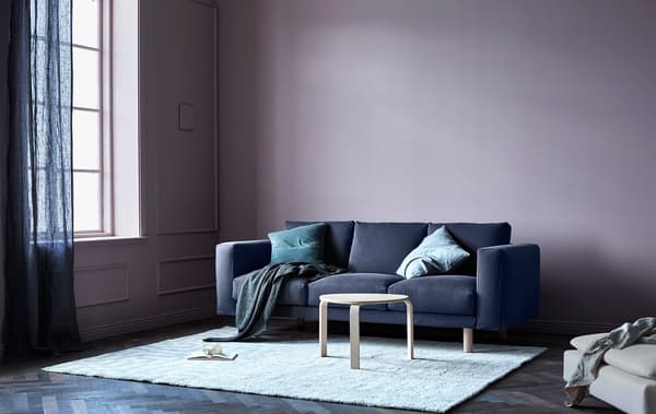 A grey sofa with cushions and throws in a living room with pink walls.