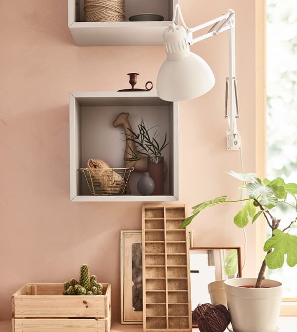 A grey, square EKET cabinet, mounted on the wall in a pink living room, being used to store and display favourite items.