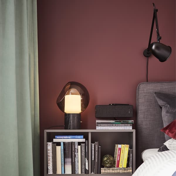 A grey table lamp in glass and brass, a grey divan bed, a black wall lamp and a dark grey cabinet.
