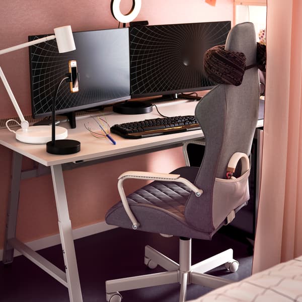 A grey UTESPELARE gaming chair in front of a light grey desk holding two monitors, a work lamp, a ring light and keyboard.