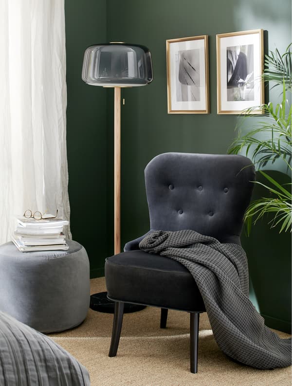 A grey velvet armchair, a grey floor lamp, a dark grey pouffe, a grey throw and gold-coloured frames.