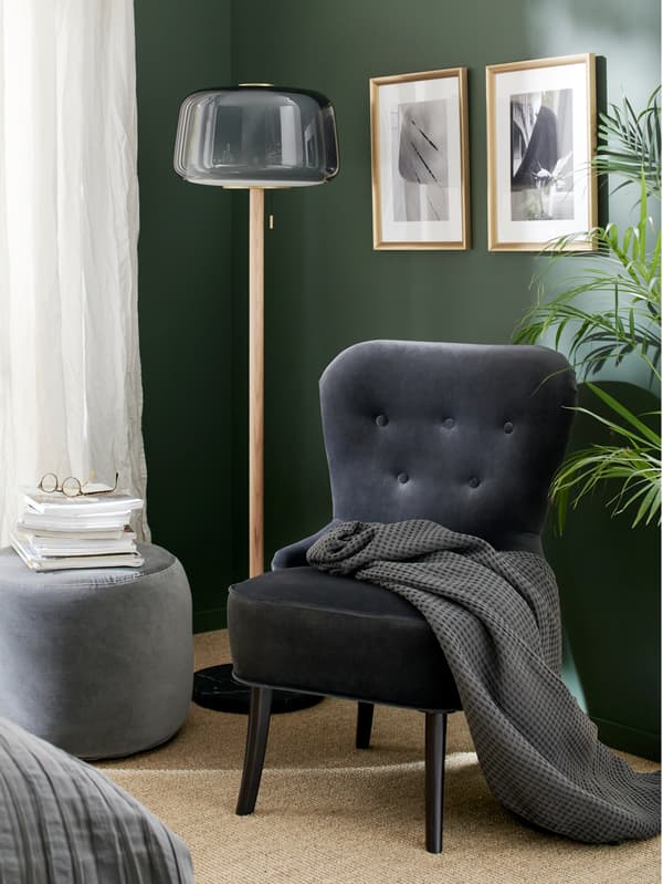 A grey velvet armchair, a grey floor lamp, a dark grey pouffe, a grey throw and gold-coloured frames.