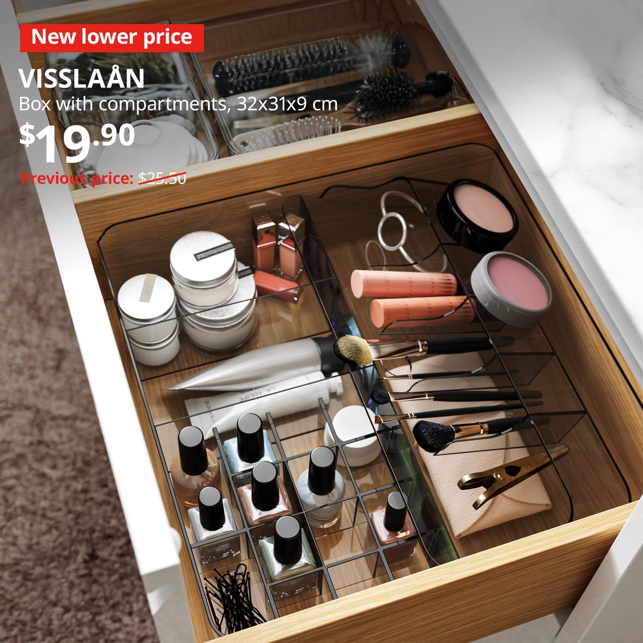 A grey VISSLAÅN box with compartments is used to organise the makeup items in the bathroom drawer in the bathroom setting. Text on image reads "New lower price, VISSLAÅN, Box with compartments, grey, 32x31x9 cm, $19.90, Previous price $69"