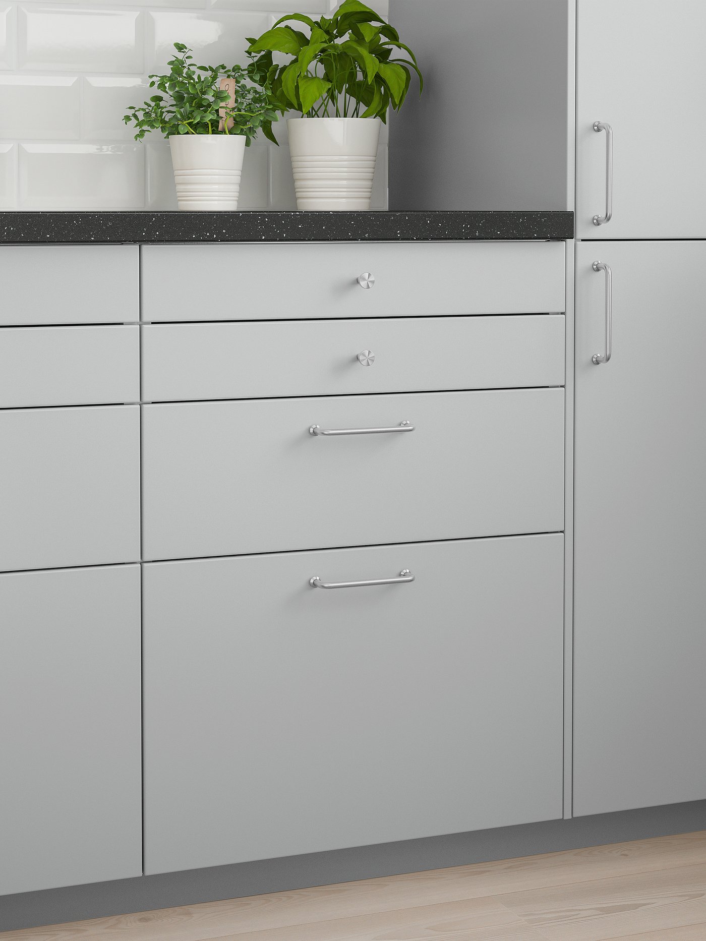 A grey wall cabinet with two doors, a black mineral-effect worktop with two plants on top and eight grey drawers below.