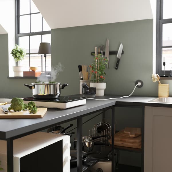 A grey worktop with a black/white portable induction hob, a pot in stainless steel, a chopping board and some broccoli.