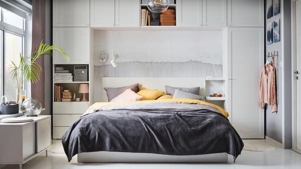 A grey, yellow and pink themed bedroom, where the bed is framed with white units from the IKEA PLATSA wardrobe series.
