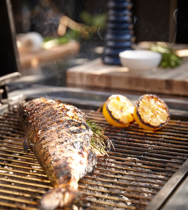 A grill with a whole fish and a couple of lemons cooking on top.