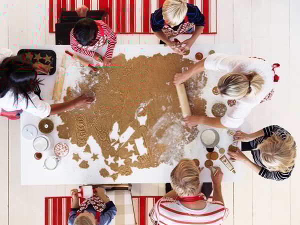 A group of children and adults make gingerbread biscuits around a huge piece of dough on a kitchen table.
