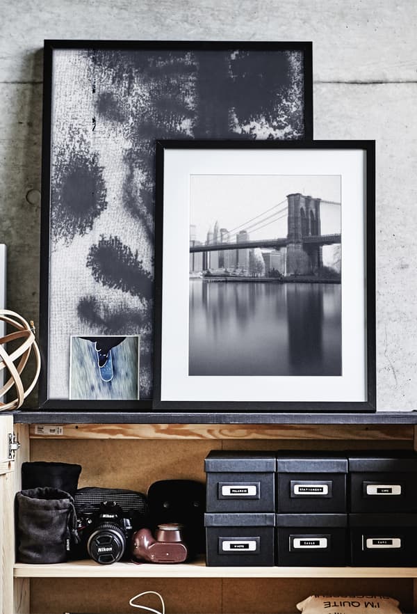 A group of framed pictures leaning against a grey wall.