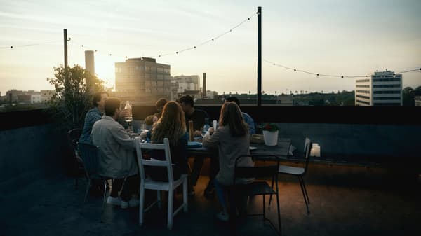 A group of friends gathered around a rooftop table at sunset.