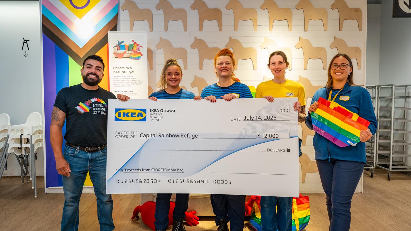 A group of IKEA coworkers are holding a large cheque in an IKEA Swedish Restaurant. 