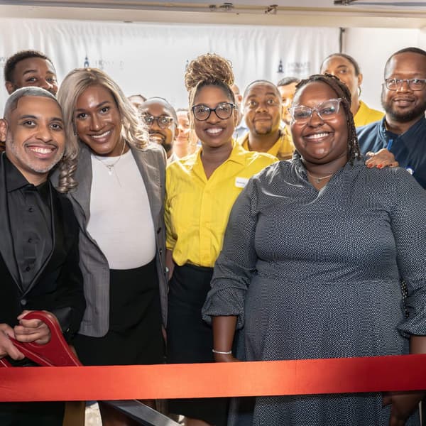 A group of people smiling with a red ribbon in front of them.